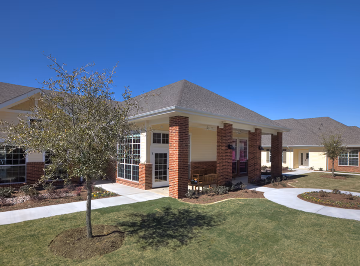 Single-story brick and siding building with a covered porch, benches, walkways, and landscaped lawn under a clear blue sky.