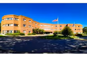 Exterior view of a curved brick senior care building with flagpole and landscaping.