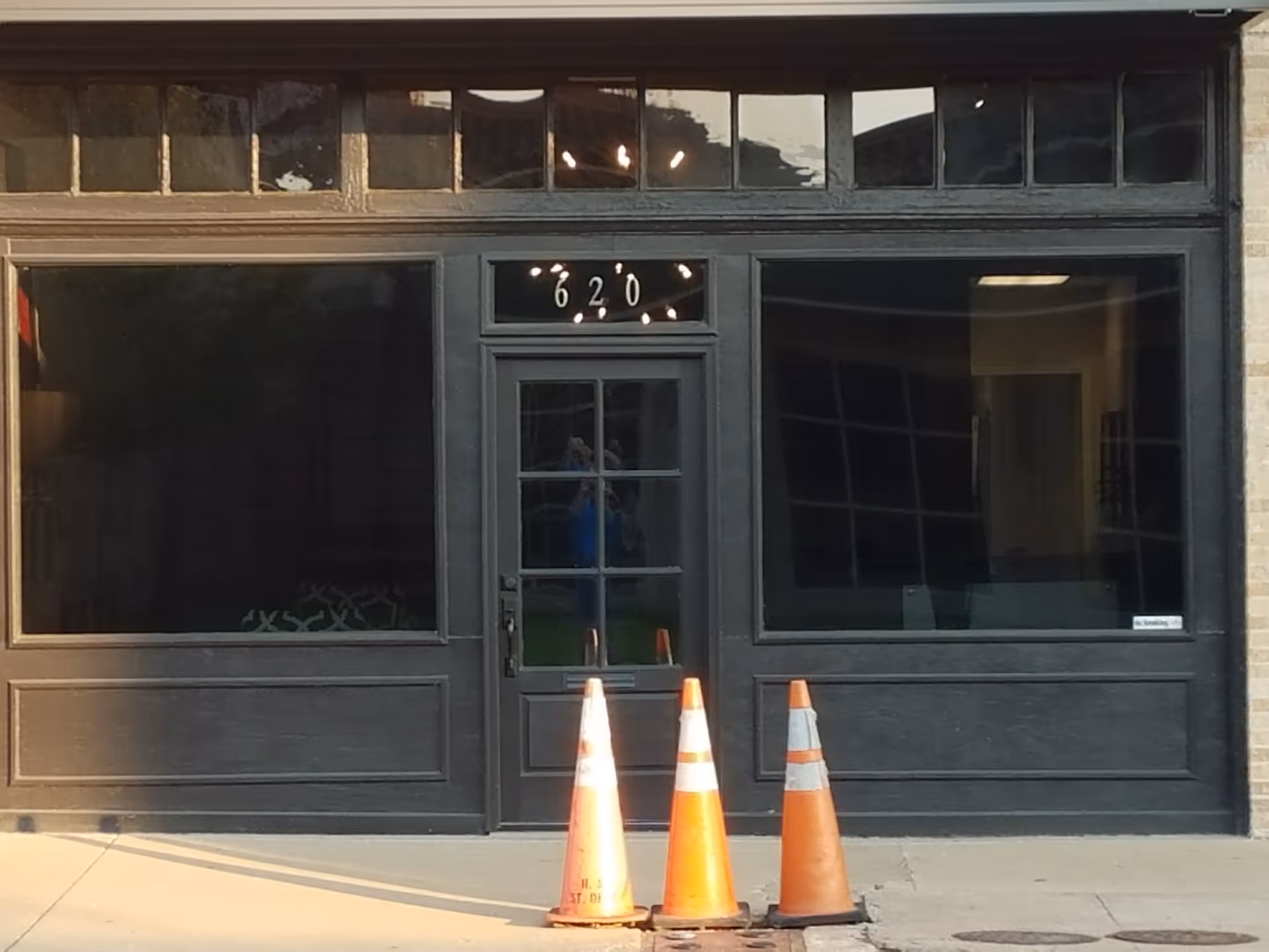Dark storefront entrance with large windows, door numbered 620, three orange traffic cones outside.