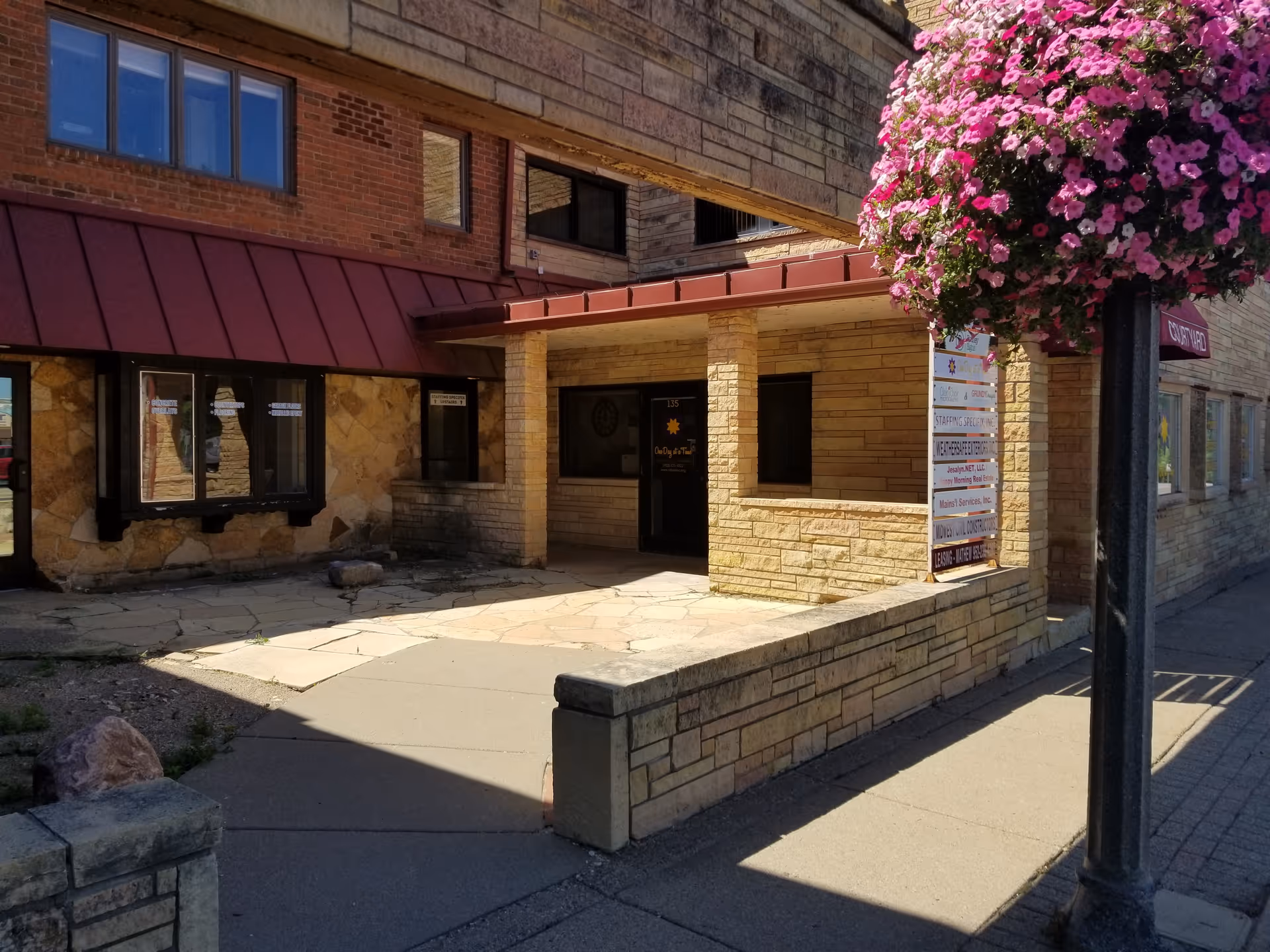 Exterior view of a senior living facility entrance with stone walls and hanging flower basket.