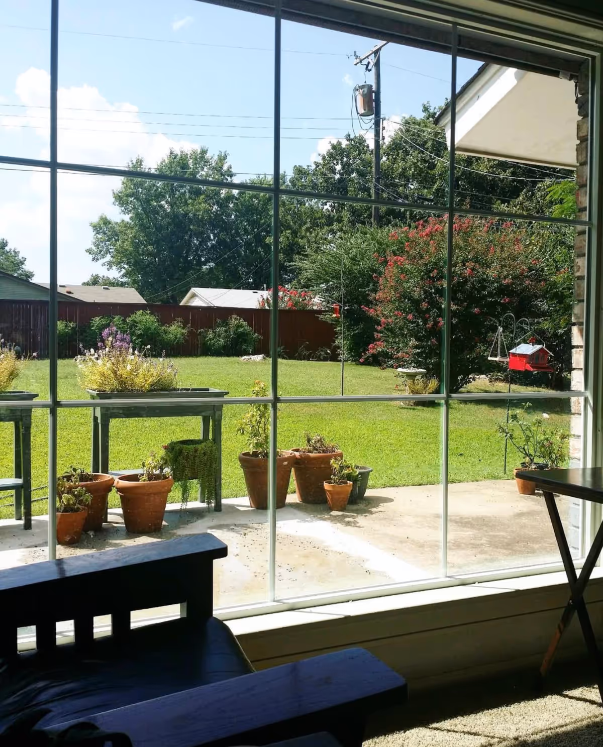 Interior room with large window, bench seating, and potted plants overlooking a sunny green backyard.