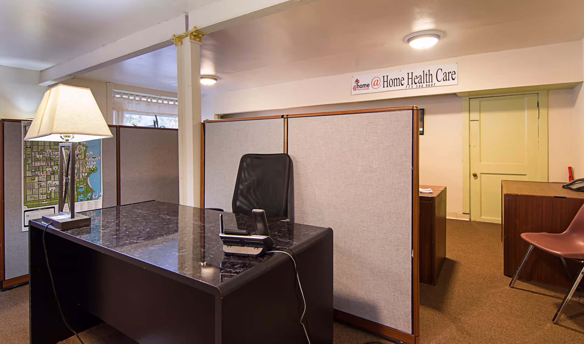 Office reception area with a dark marble desk, lamp, and partitioned cubicles.