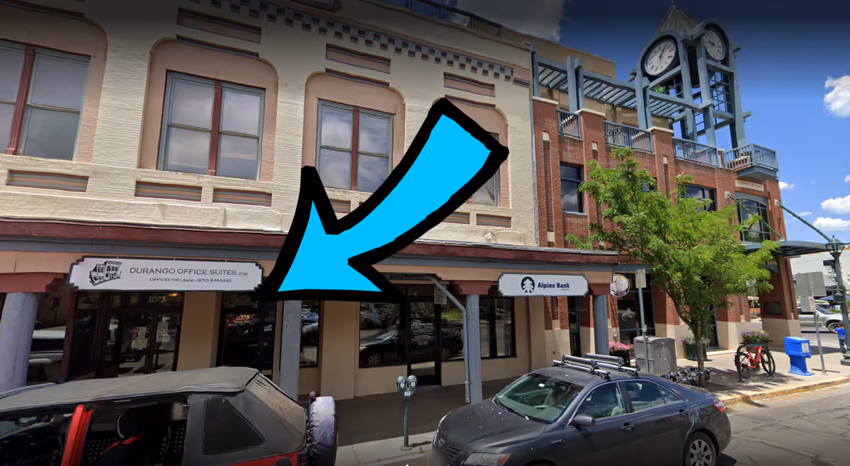 Brick storefront building on a city street with signs and parked cars.