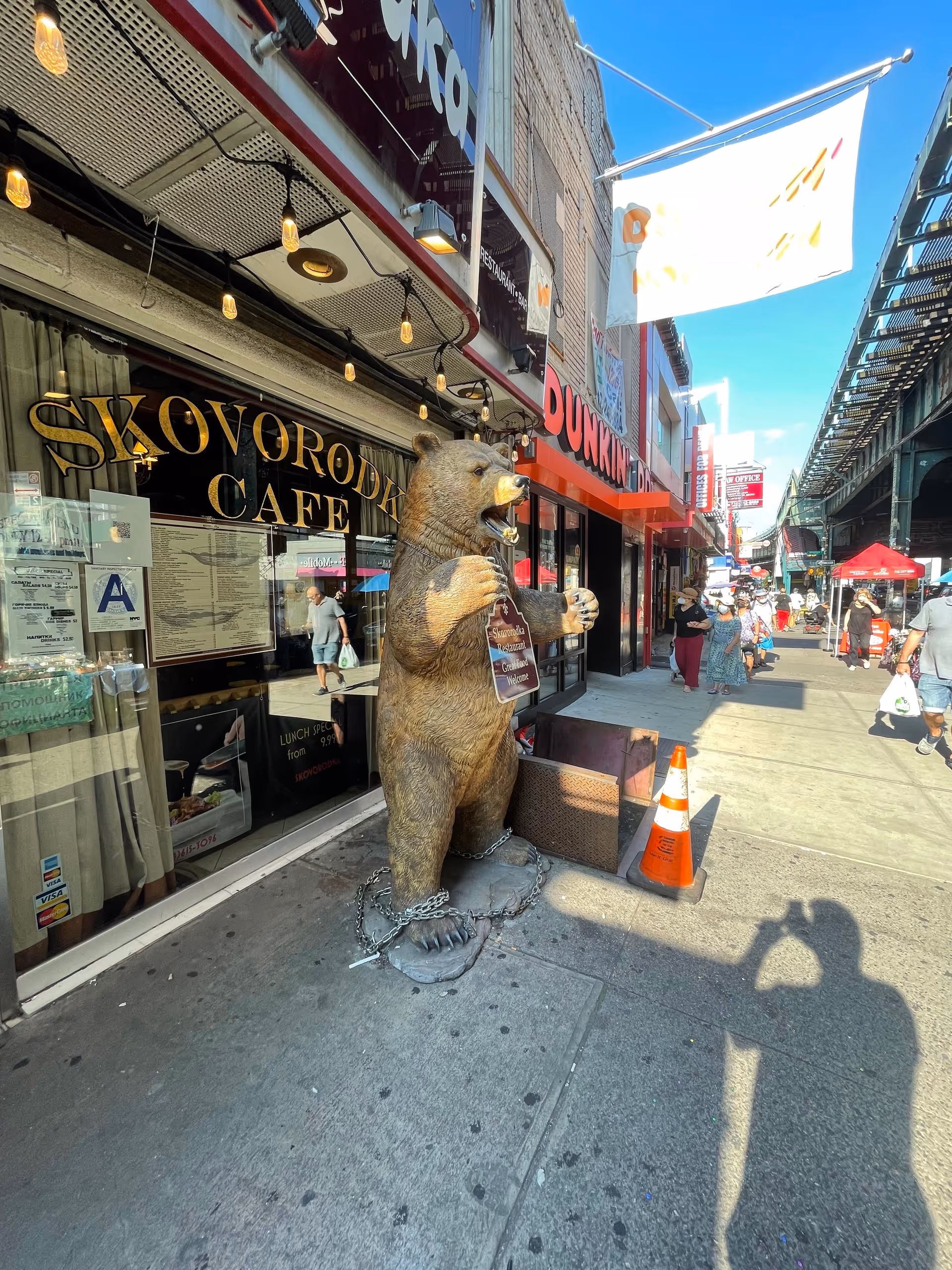 Urban sidewalk with a large bear statue in front of a cafe and shops