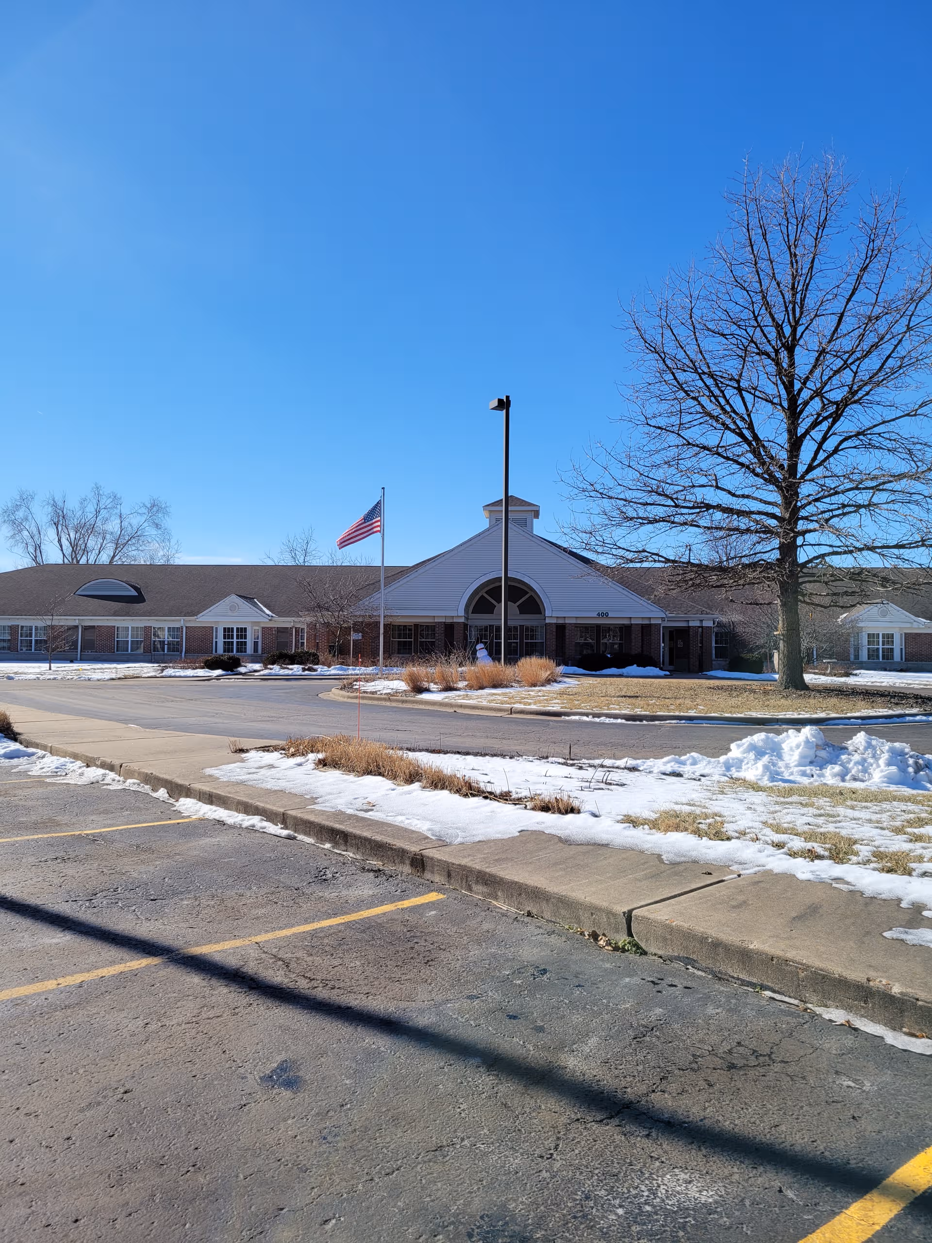 Exterior view of Country Gardens senior living facility with flag, entrance, and snow