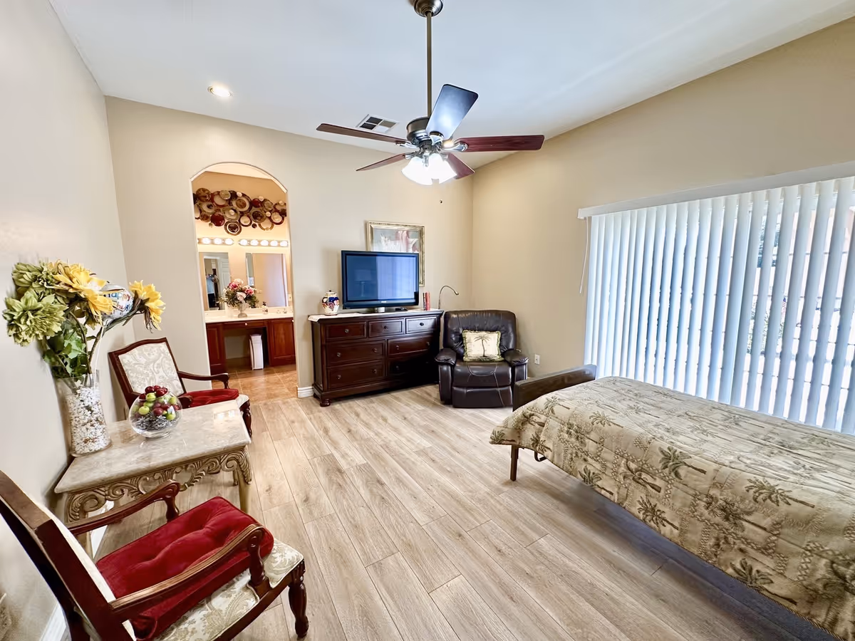 This is a spacious bedroom suite with a bed, seating area, TV, and large window blinds.