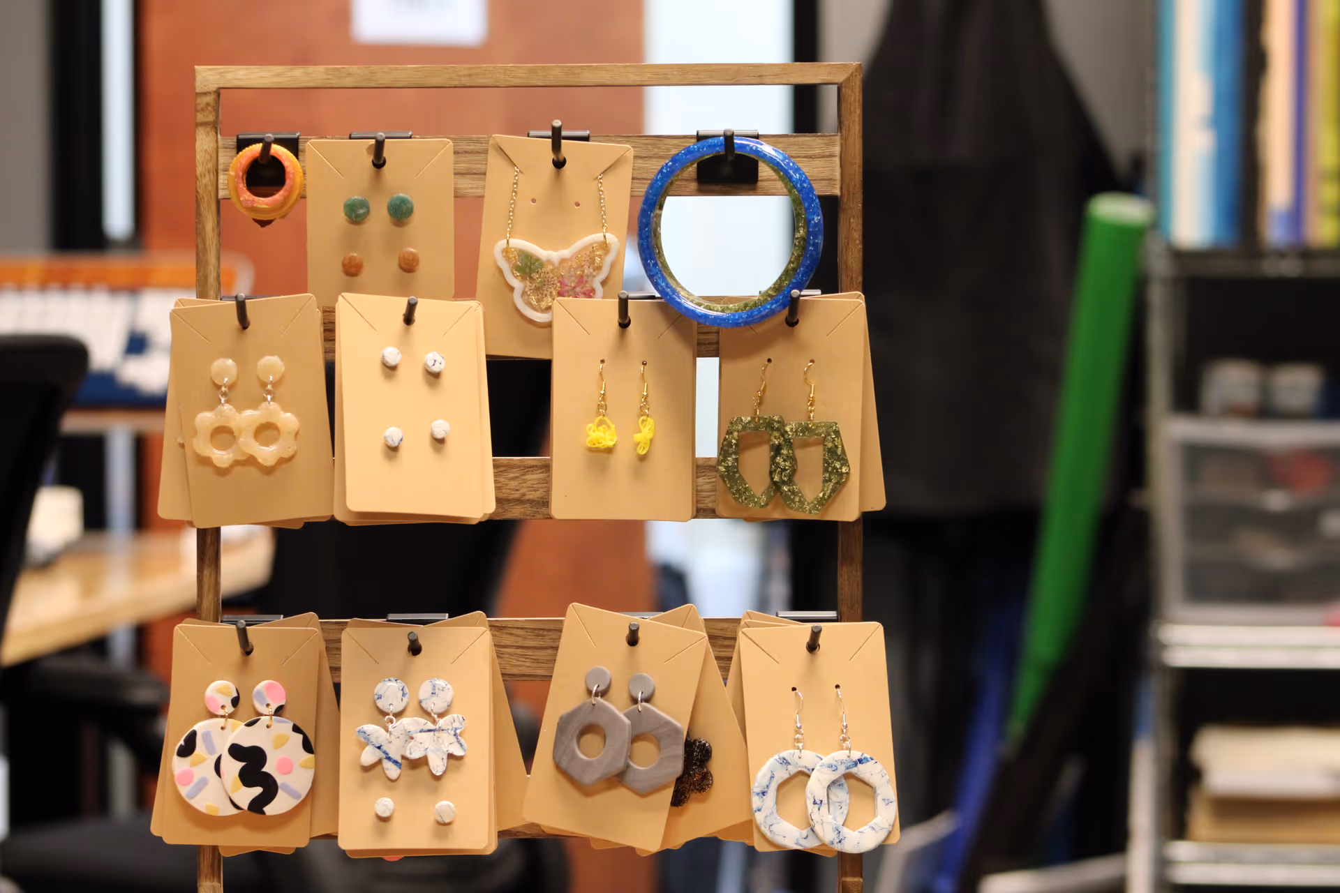 Wooden jewelry rack displays varied earrings and accessories in an indoor craft space.