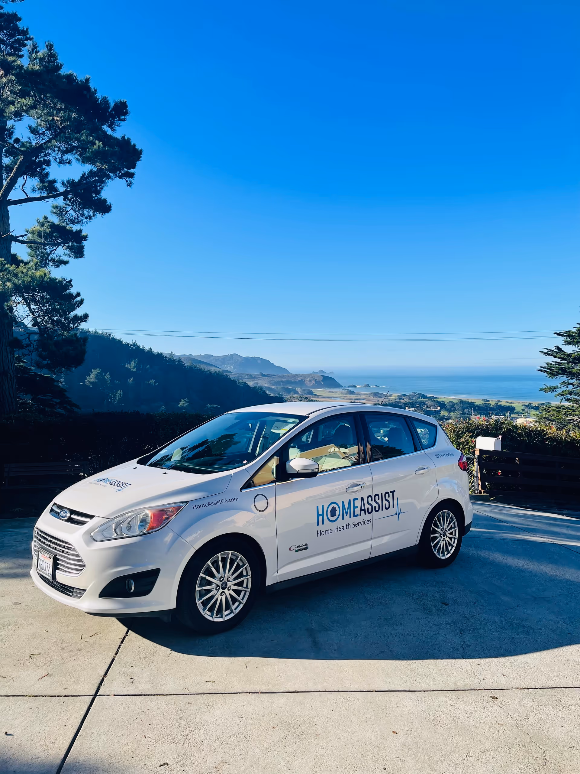 White HomeAssist vehicle parked on a driveway with a coastal landscape background.