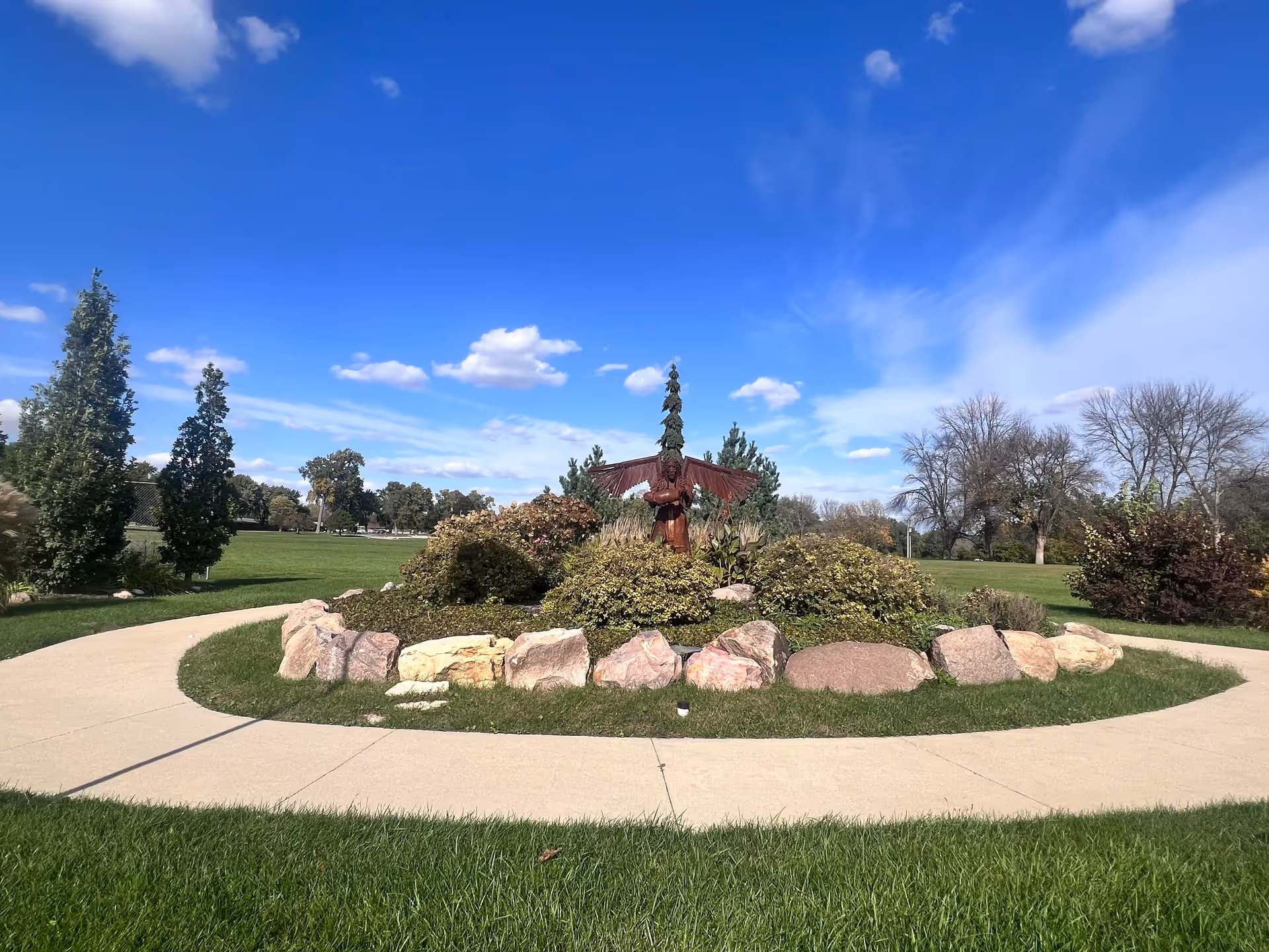 Circular garden with rock border and statue centerpiece under blue sky.