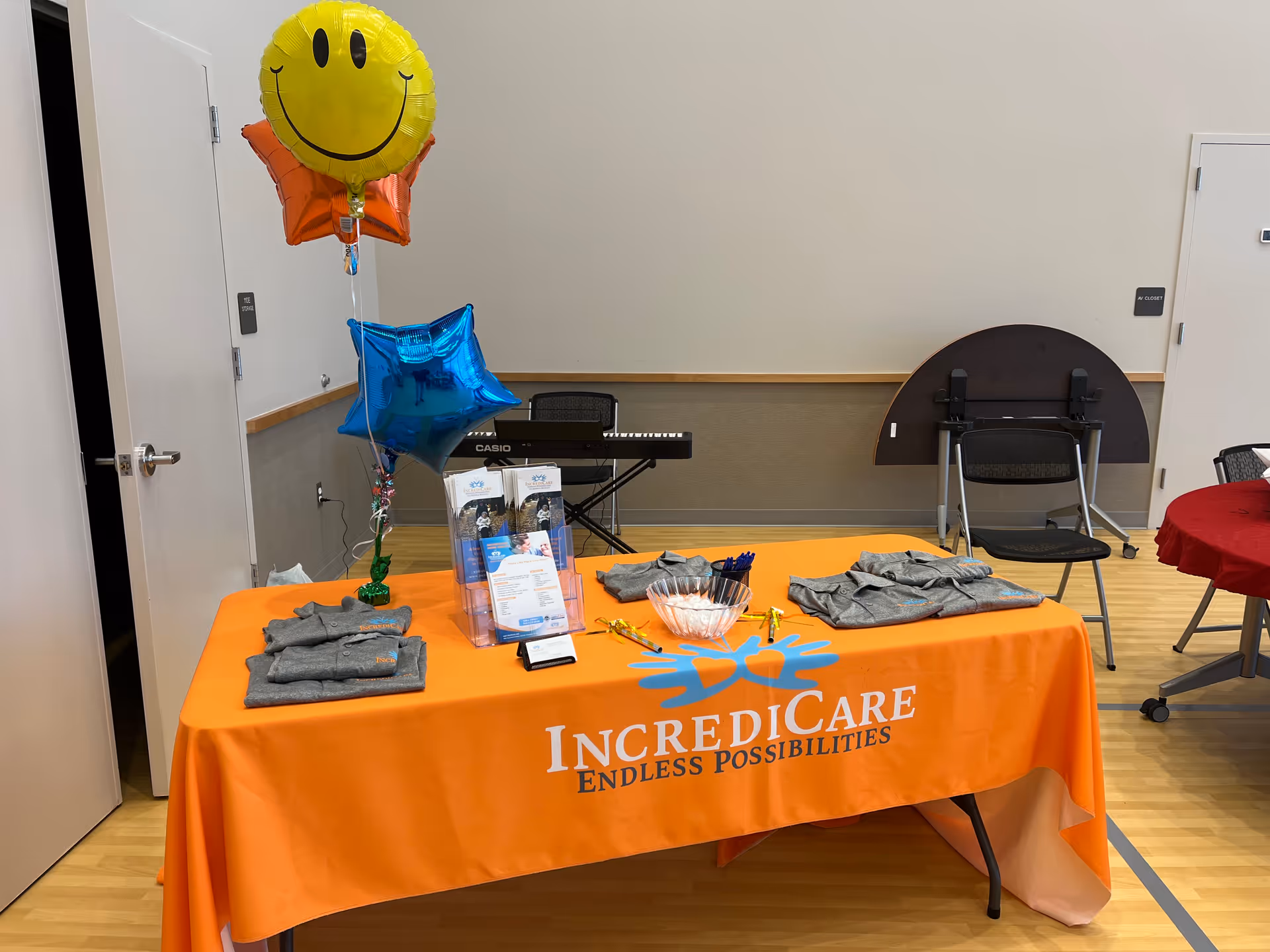 Orange table with IncrediCare logo, balloons, brochures, and a keyboard in a bright interior.