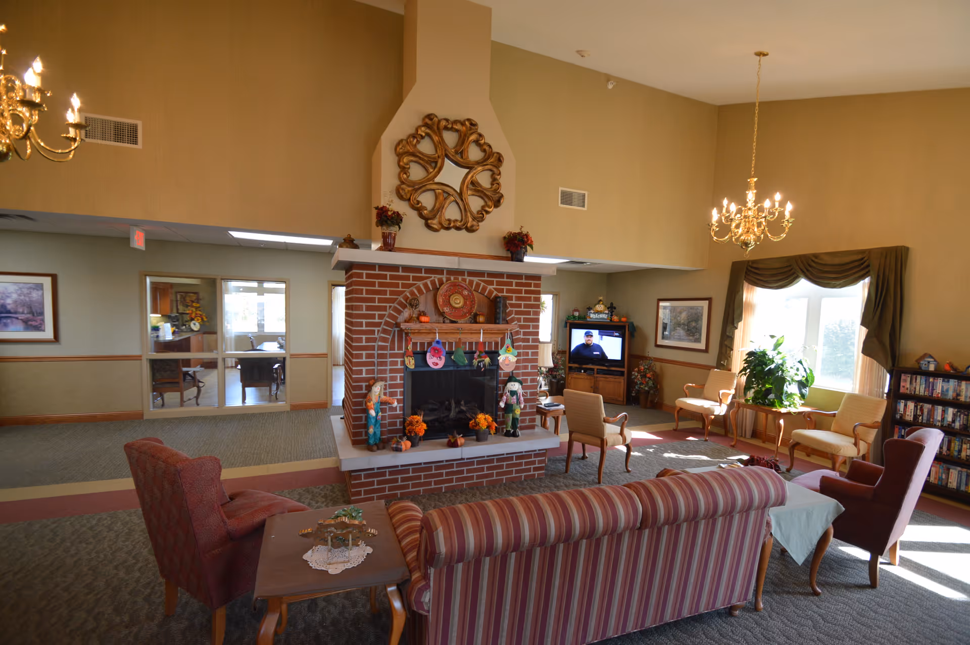 Spacious communal living room with a central brick fireplace, sofas and chairs, a TV, and chandeliers.
