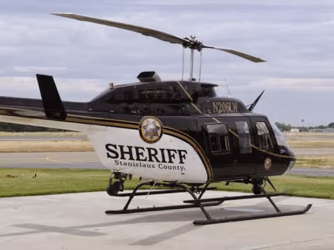 A black Sheriff helicopter parked on a concrete tarmac with grass and a cloudy sky.