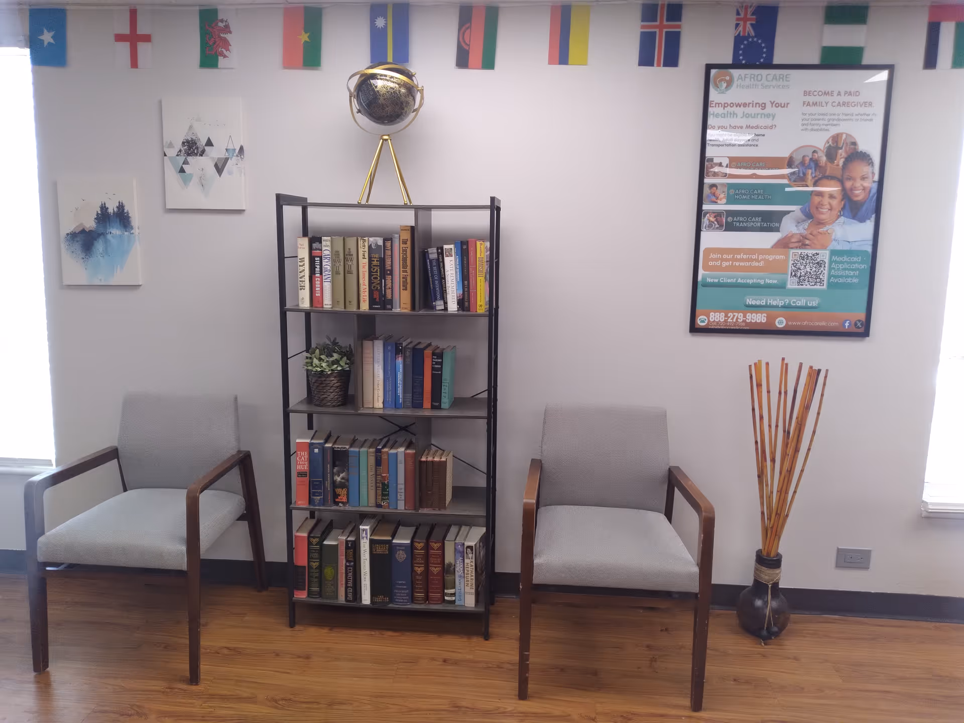 Indoor waiting area with two gray chairs, a bookshelf, poster, and decorative flags.