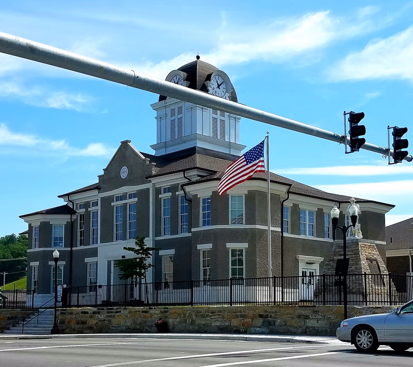 Large gray building with clock tower and American flag by a street intersection.