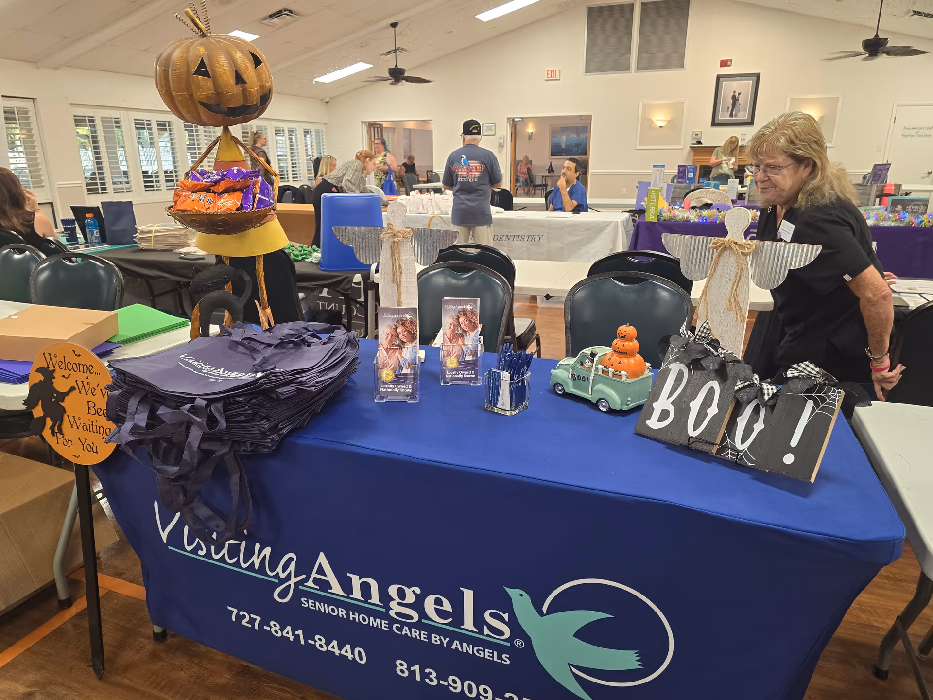 Indoor event hall with a blue Visiting Angels display table and attendees nearby.
