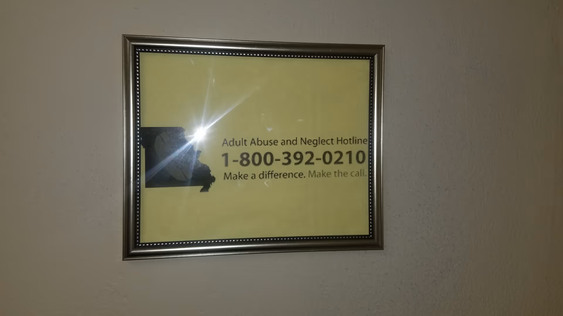 Framed yellow sign on a wall shows the Adult Abuse and Neglect Hotline number.