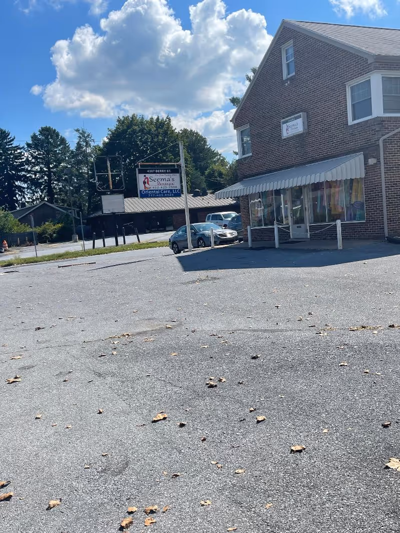 Brick storefront building with striped awning and Oriental Care, LLC sign by parking lot.