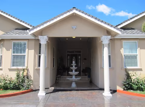 Covered front entrance of a beige building with white columns and a multi-tiered fountain in the entryway.