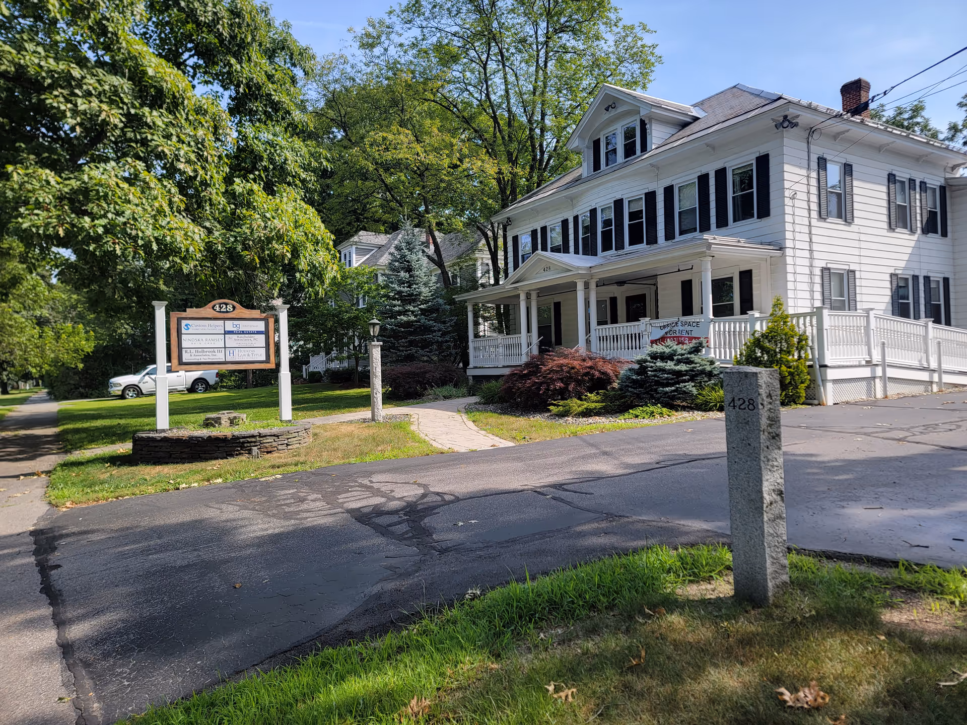 White two-story home-style senior care facility with a porch, sign, and landscaped front yard.