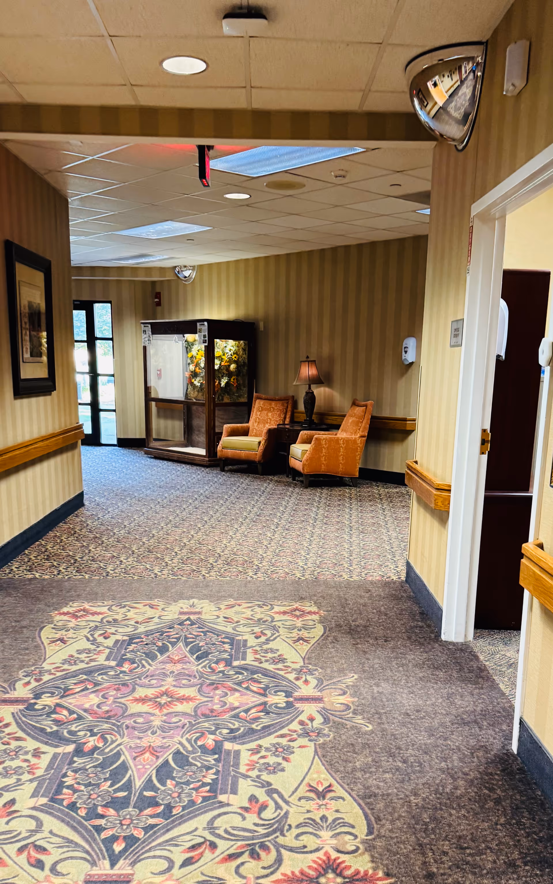 Carpeted hallway inside a senior living facility with seating area and ornate carpet pattern.