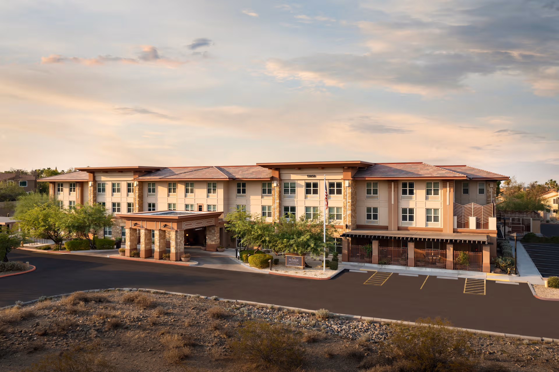 Front view of a three-story senior living building with a covered entrance and parking lot.