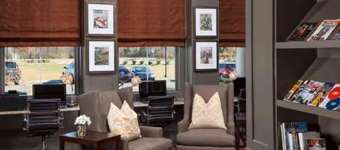 Cozy indoor lounge with two armchairs, a side table, magazines, and large windows.