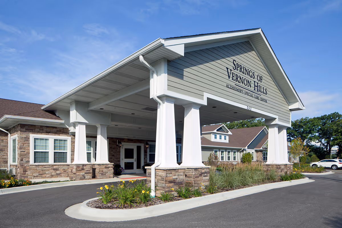 Exterior view of a senior care facility with a covered entrance and landscaping.
