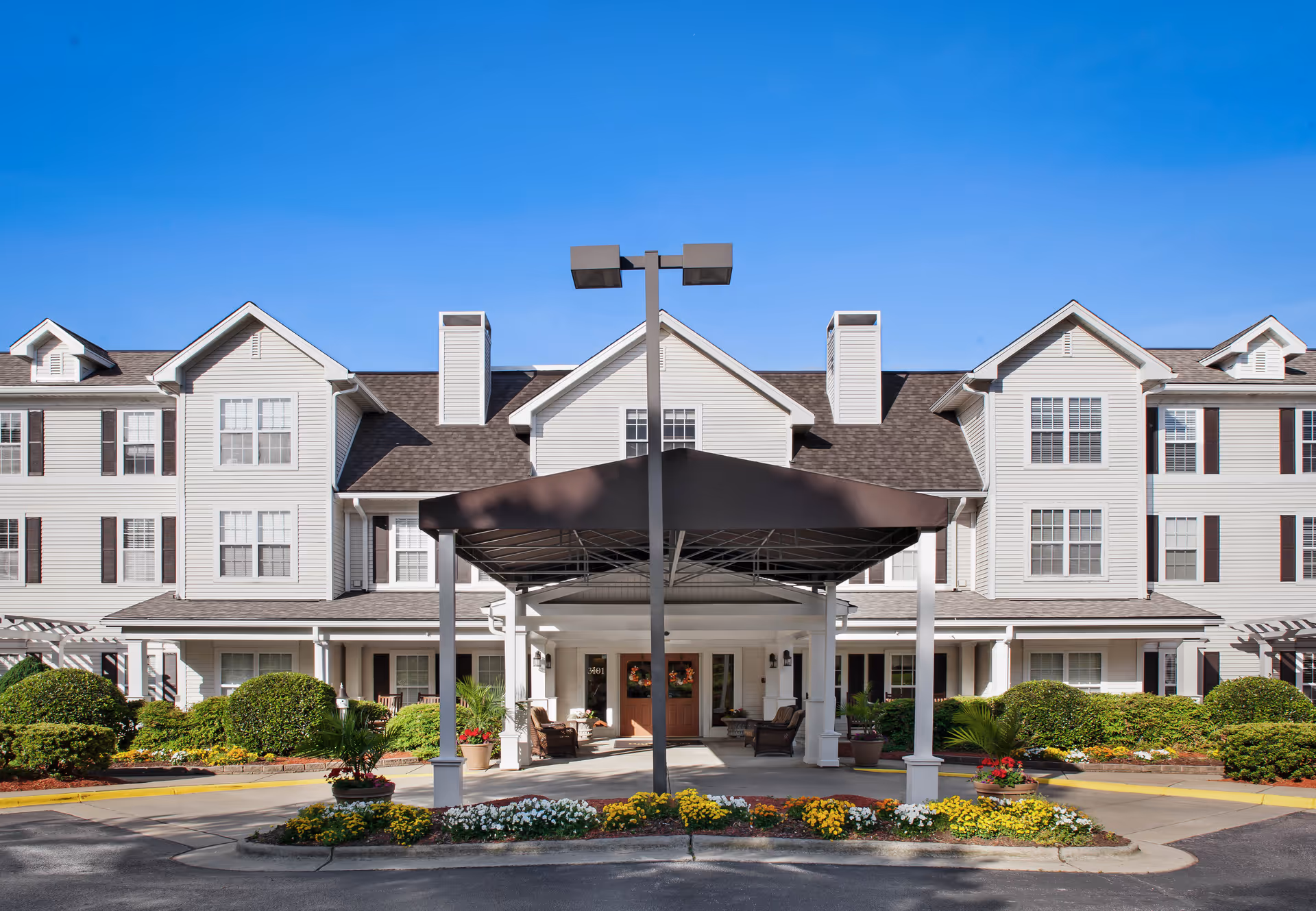 White, multi-story senior living building with a covered entrance and manicured front landscaping.