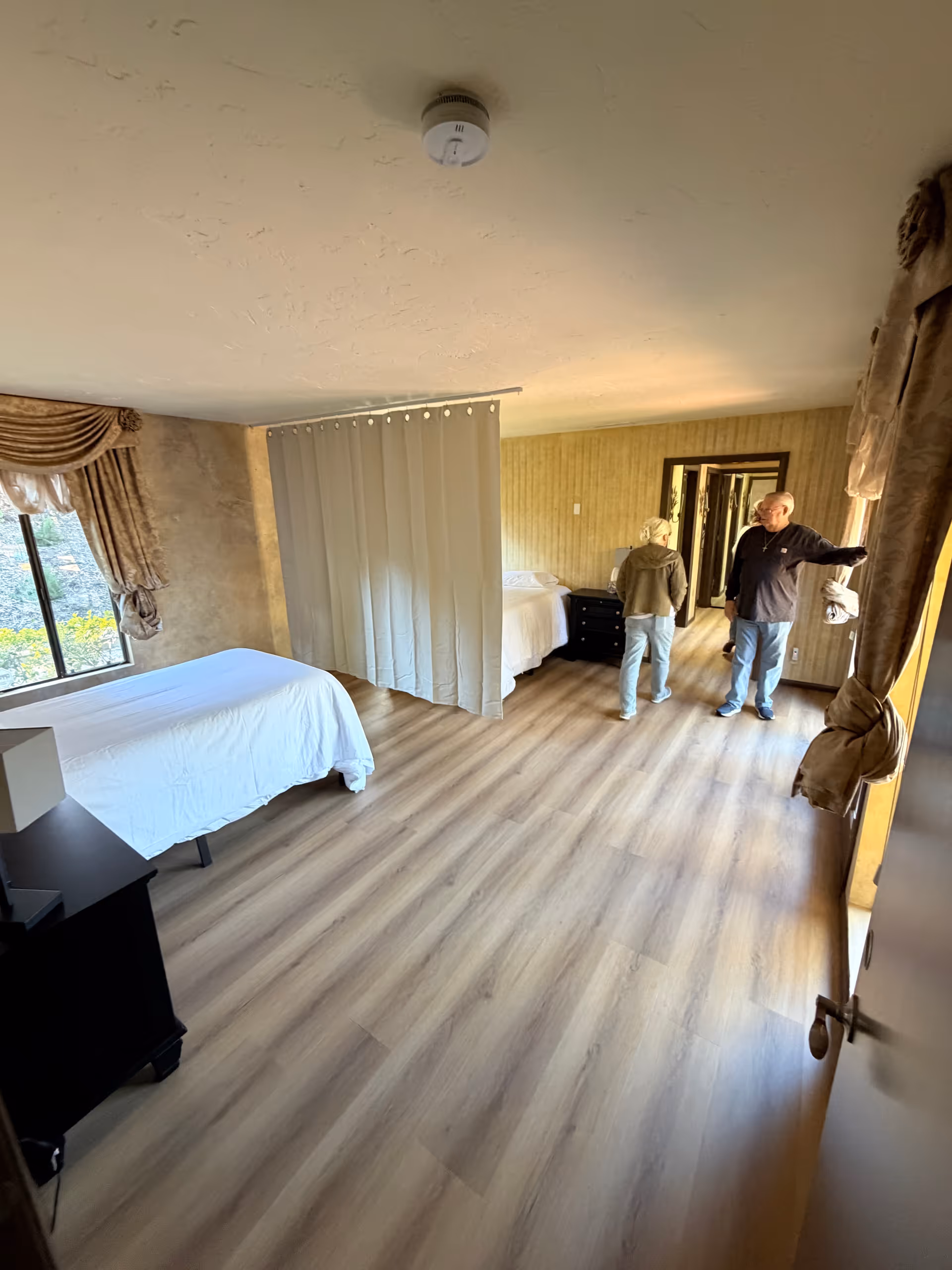 A spacious resident room with two beds separated by a privacy curtain and two people standing.