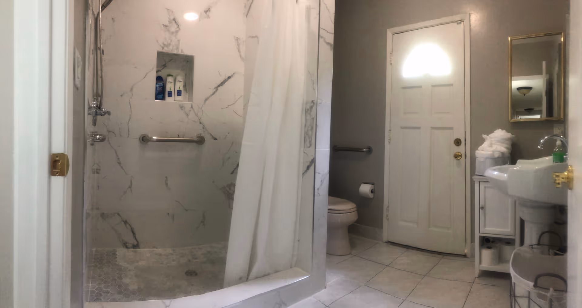 Bathroom in an assisted living facility with marble shower, curtain, toilet, sink, and mirror.