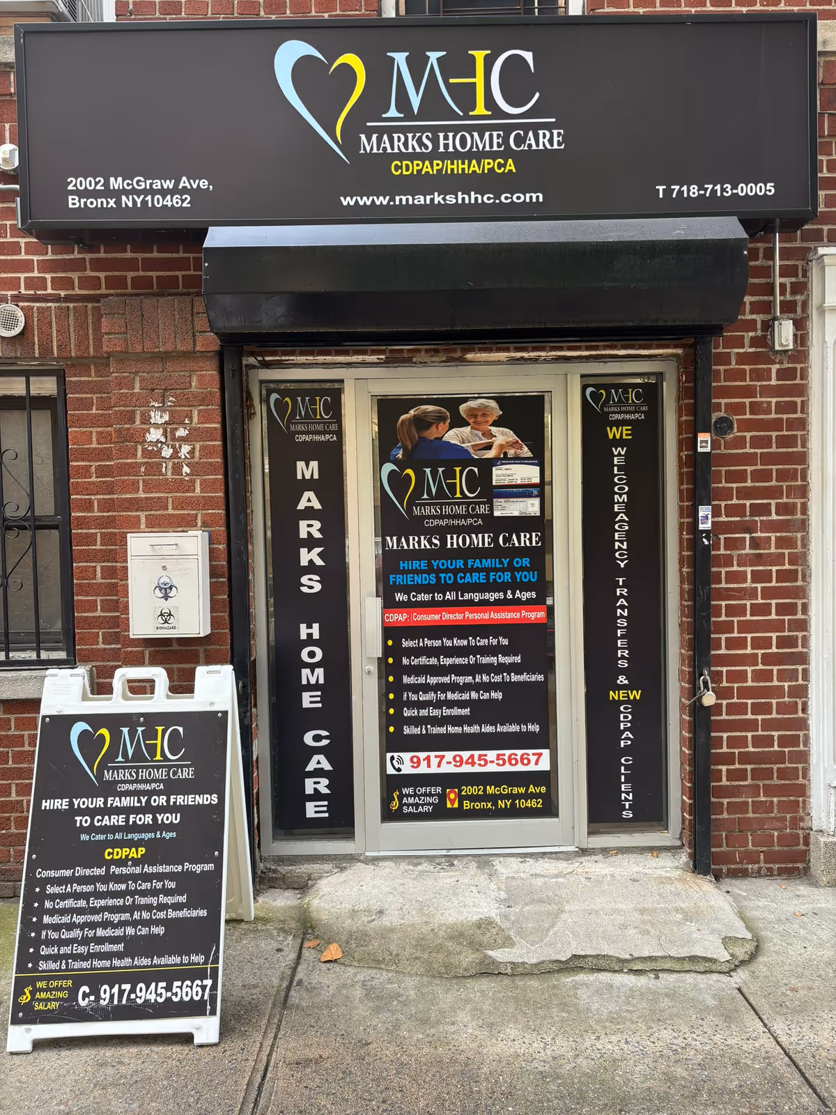 Brick building storefront with large Marks Home Care sign and glass door displaying posters.