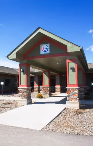 Front entrance of a senior living facility with stone columns and a green-red roof.