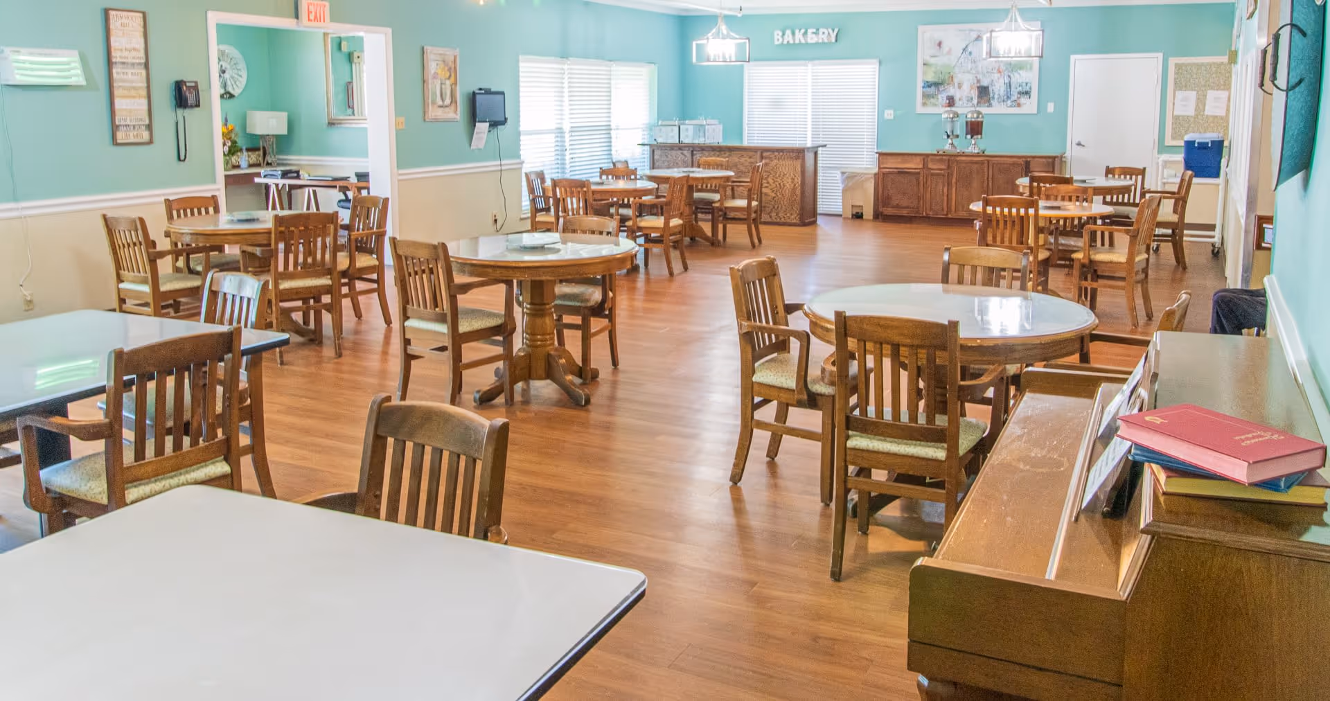 Communal dining room with round tables and wooden chairs in pastel-walled setting.