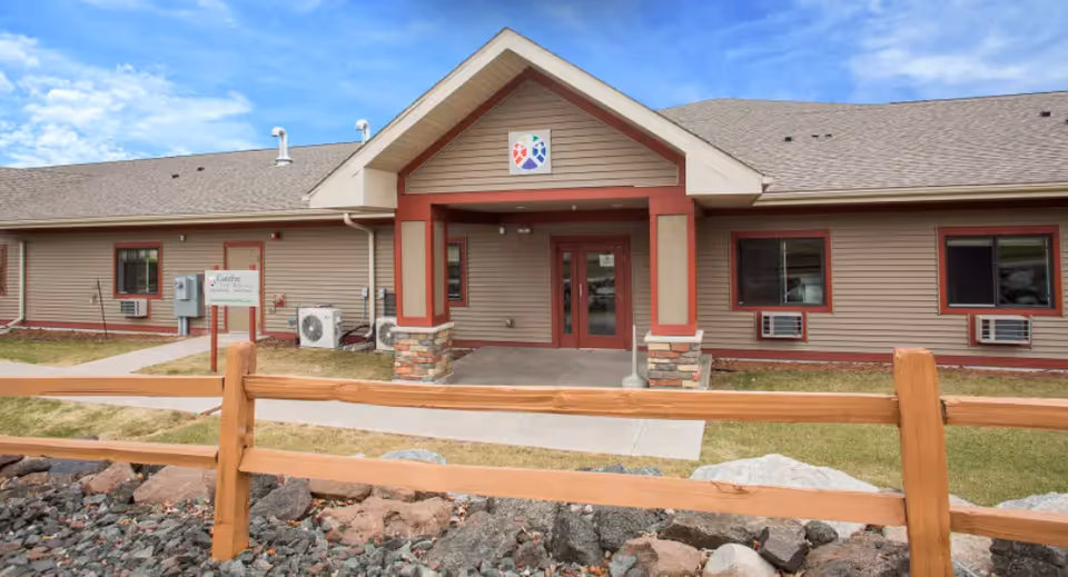 Single-story beige care facility with red trim and a wooden fence in front.