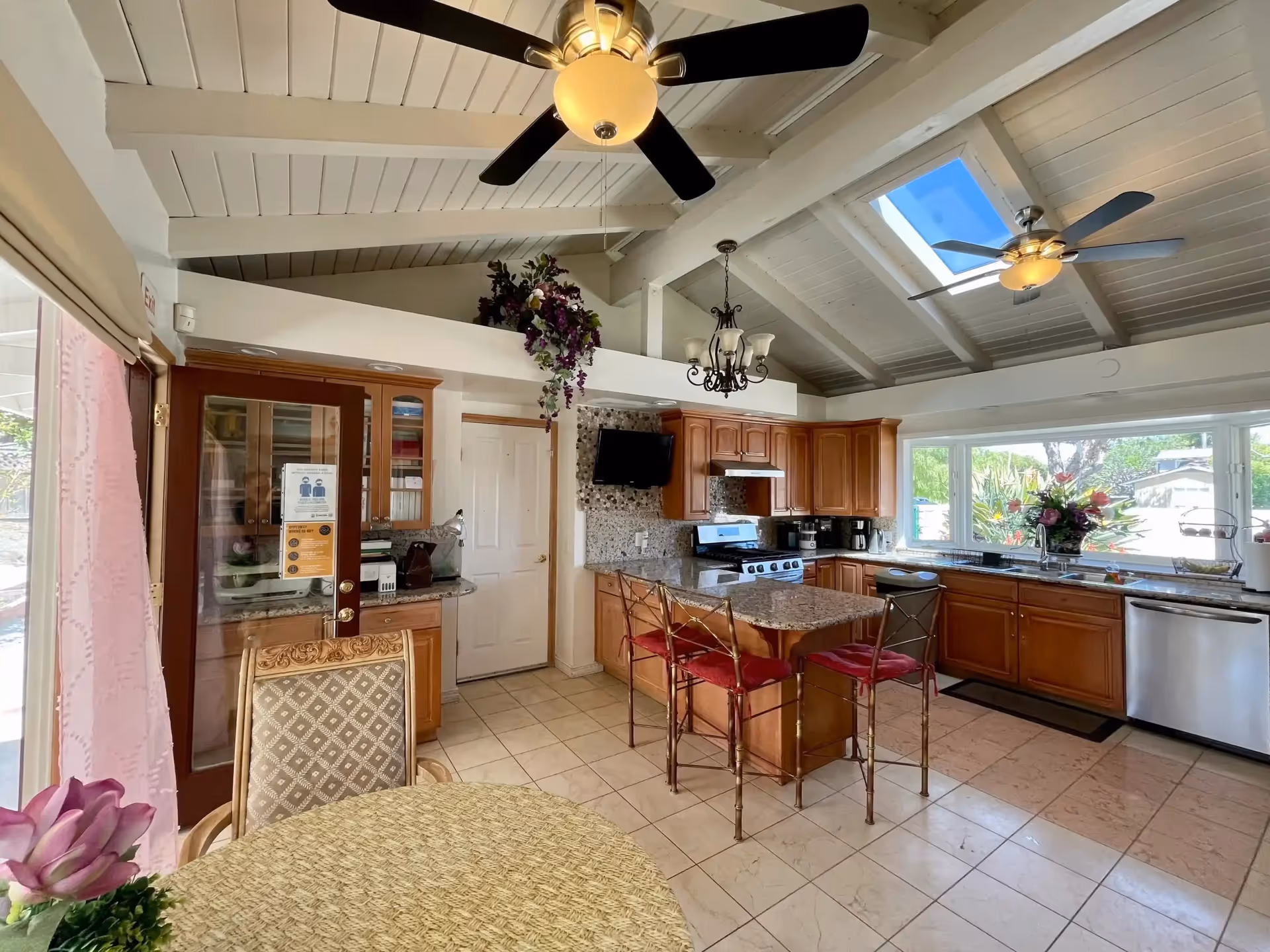 Bright open kitchen with wooden cabinets, island, skylights, ceiling fans, and dining table.
