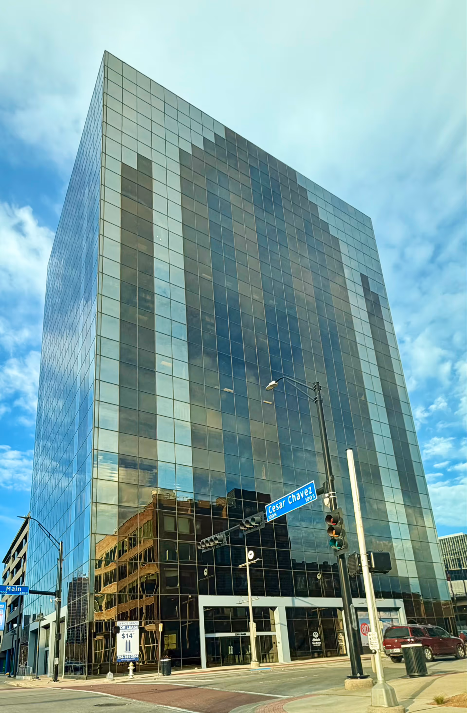 Tall glass-front building on a city street beneath a blue sky.