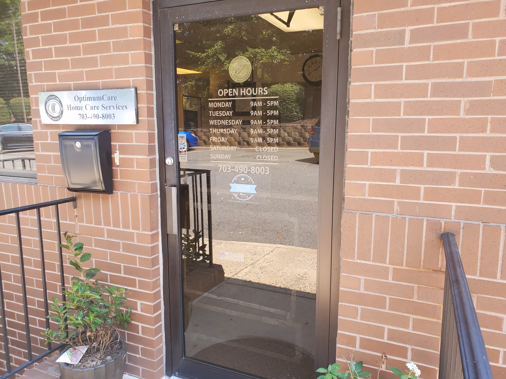 Brick exterior entrance with glass door and OptimumCare signage; open hours posted.