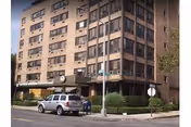 Multi-story brick nursing home building with parked cars along a street corner.