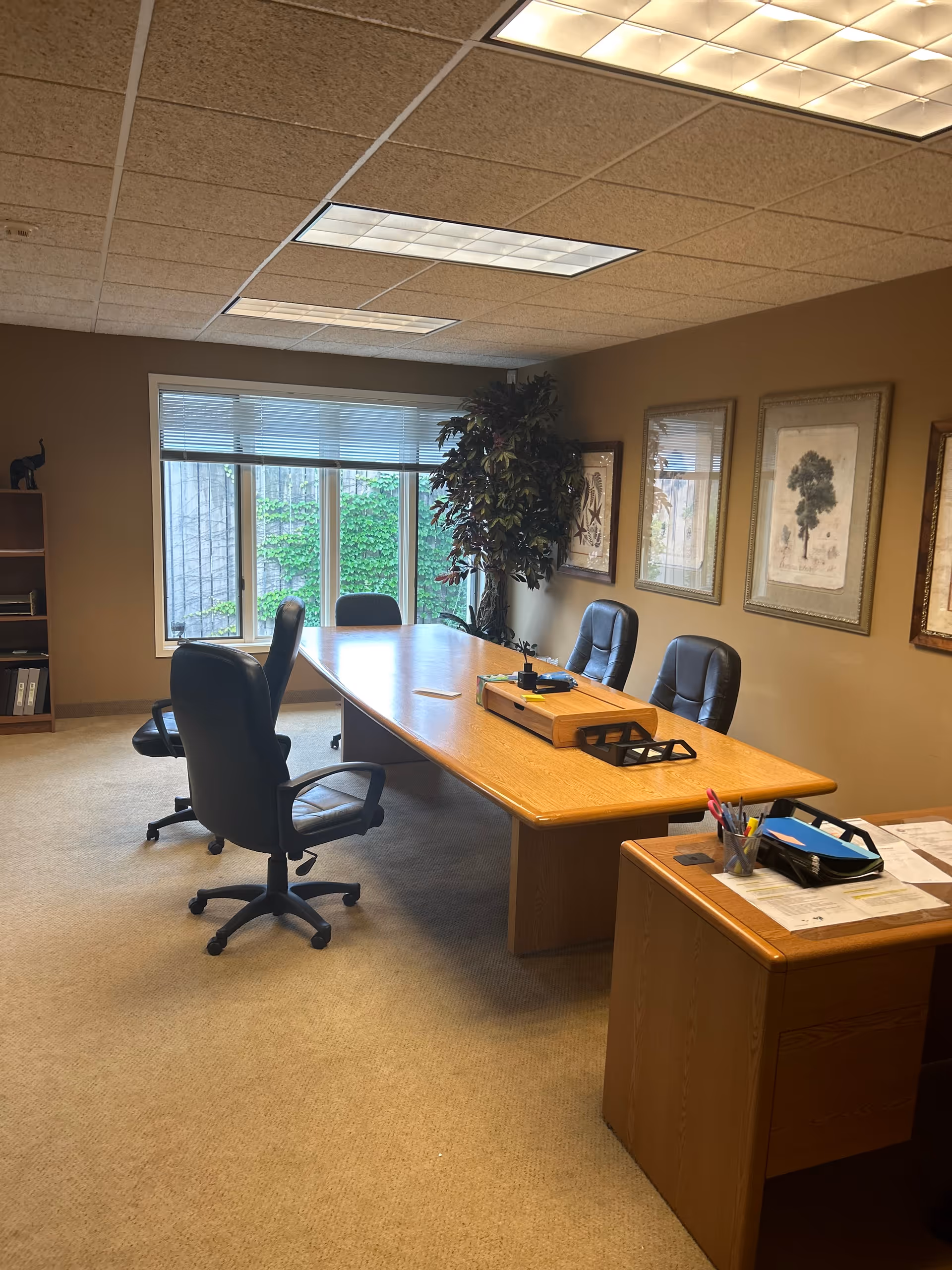 Conference room with a long wooden table, black chairs, and framed artwork on beige walls.
