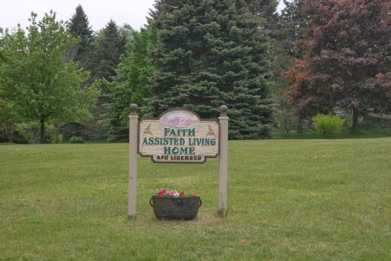 Sign reading Faith Assisted Living Home AFC Licensed on grassy lawn with trees