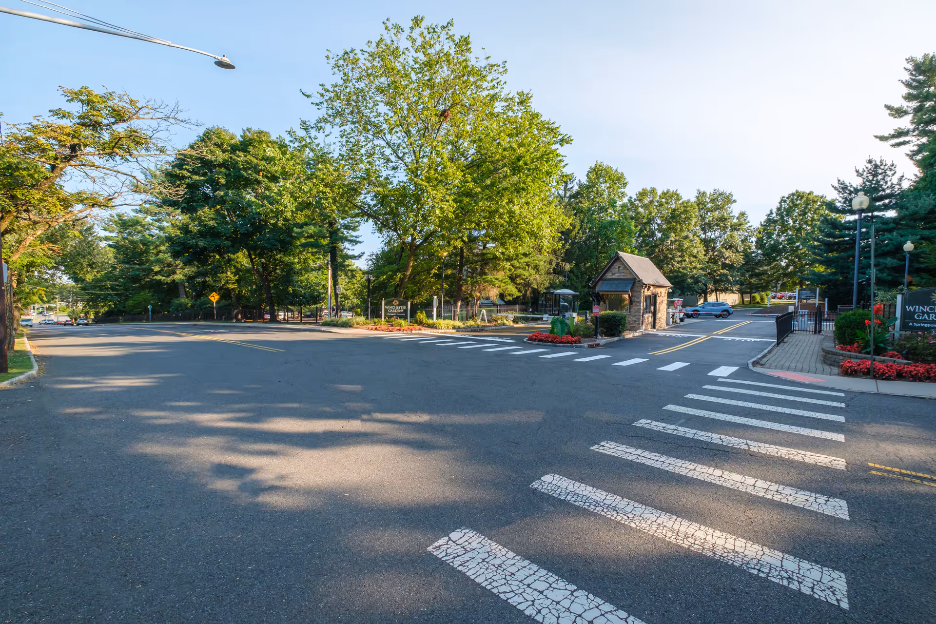 Entrance to Winchester Gardens with a gated guardhouse, crosswalk, and tree-lined driveway.