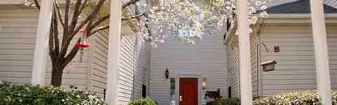 White exterior building entrance with blooming tree, pillars, and a red front door.