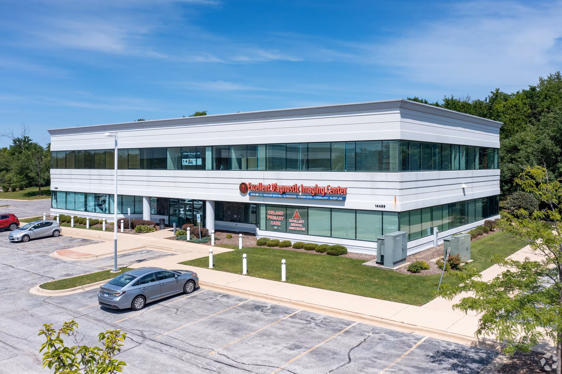 Modern two-story medical building with glass windows and a parking lot in front.