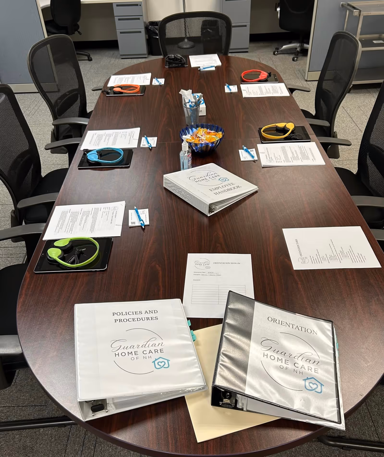 Long conference table with documents and binders labeled Guardian Home Care of NH in meeting room.