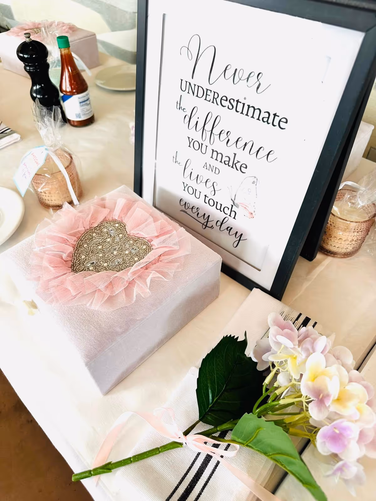 Decorative table setup with a framed quote, pink gift box, and flowers.