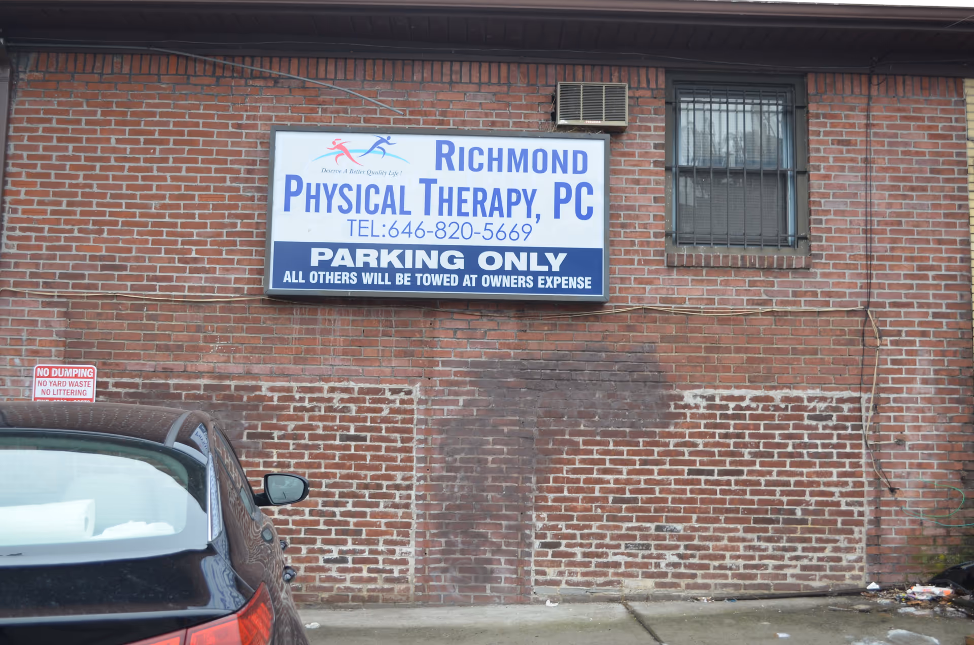 Brick exterior of Richmond Physical Therapy clinic with a large sign and a parked car.