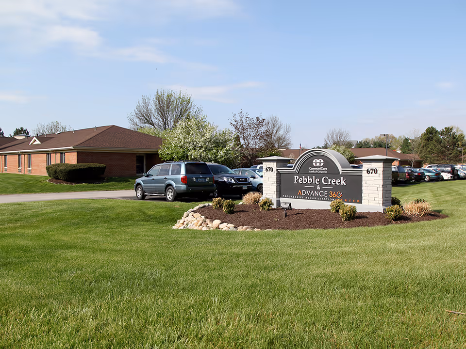Pebble Creek sign with landscaping and parked cars in front of a brick facility.