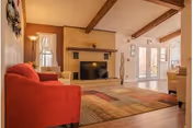 Cozy living room with a brick fireplace, red sofa, beige chairs, and wooden beams.
