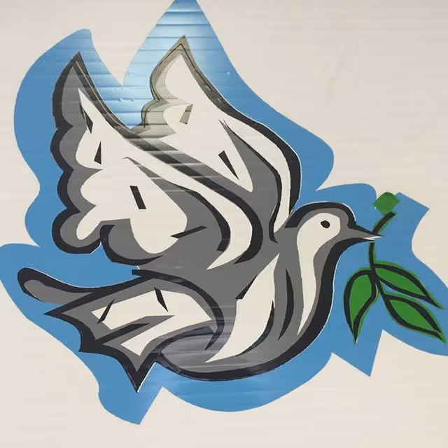 Graffiti mural of a gray dove holding a green leaf on a light wall.