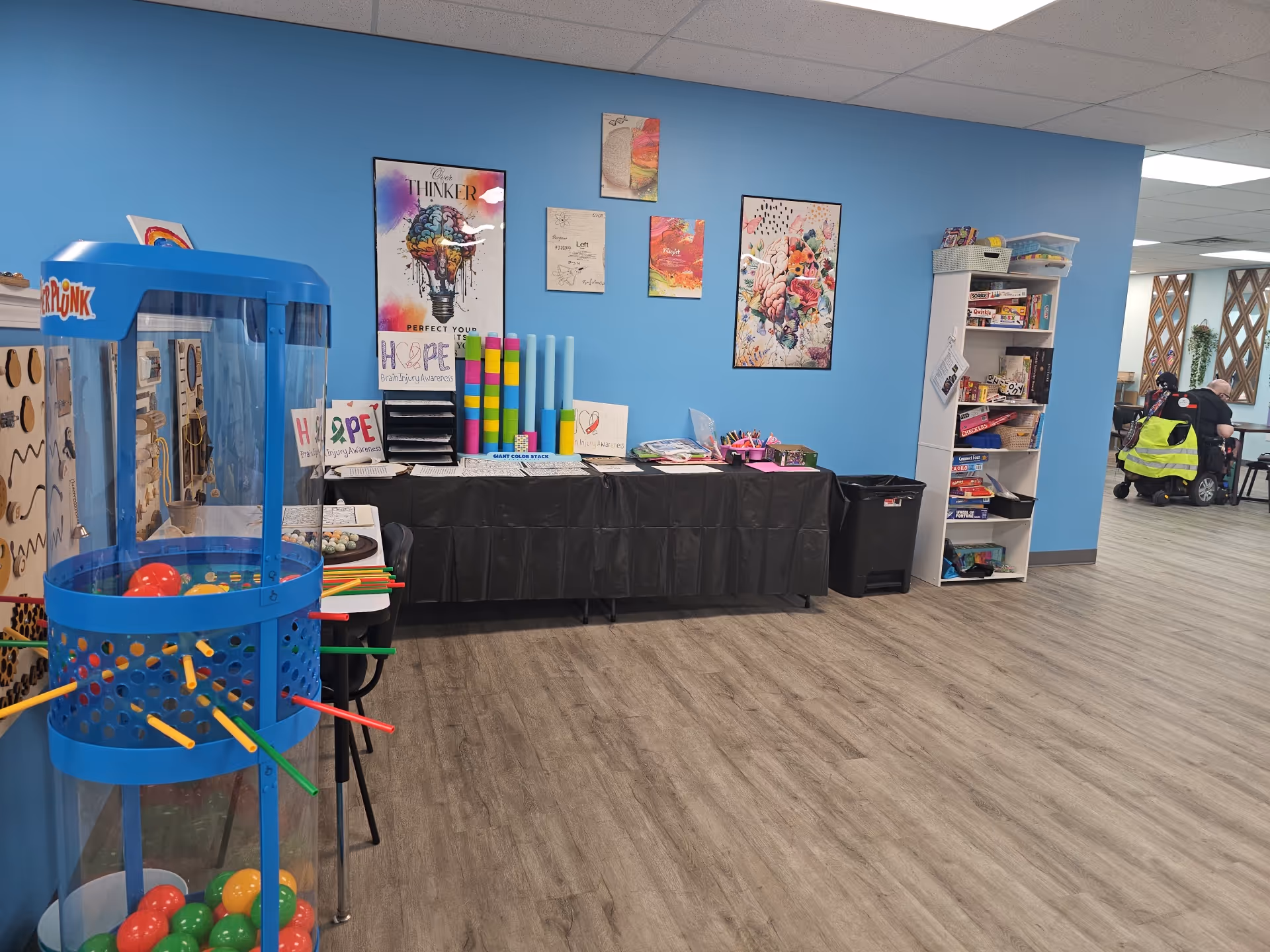 Bright blue-walled recreation area with craft table, shelves, and arcade game.